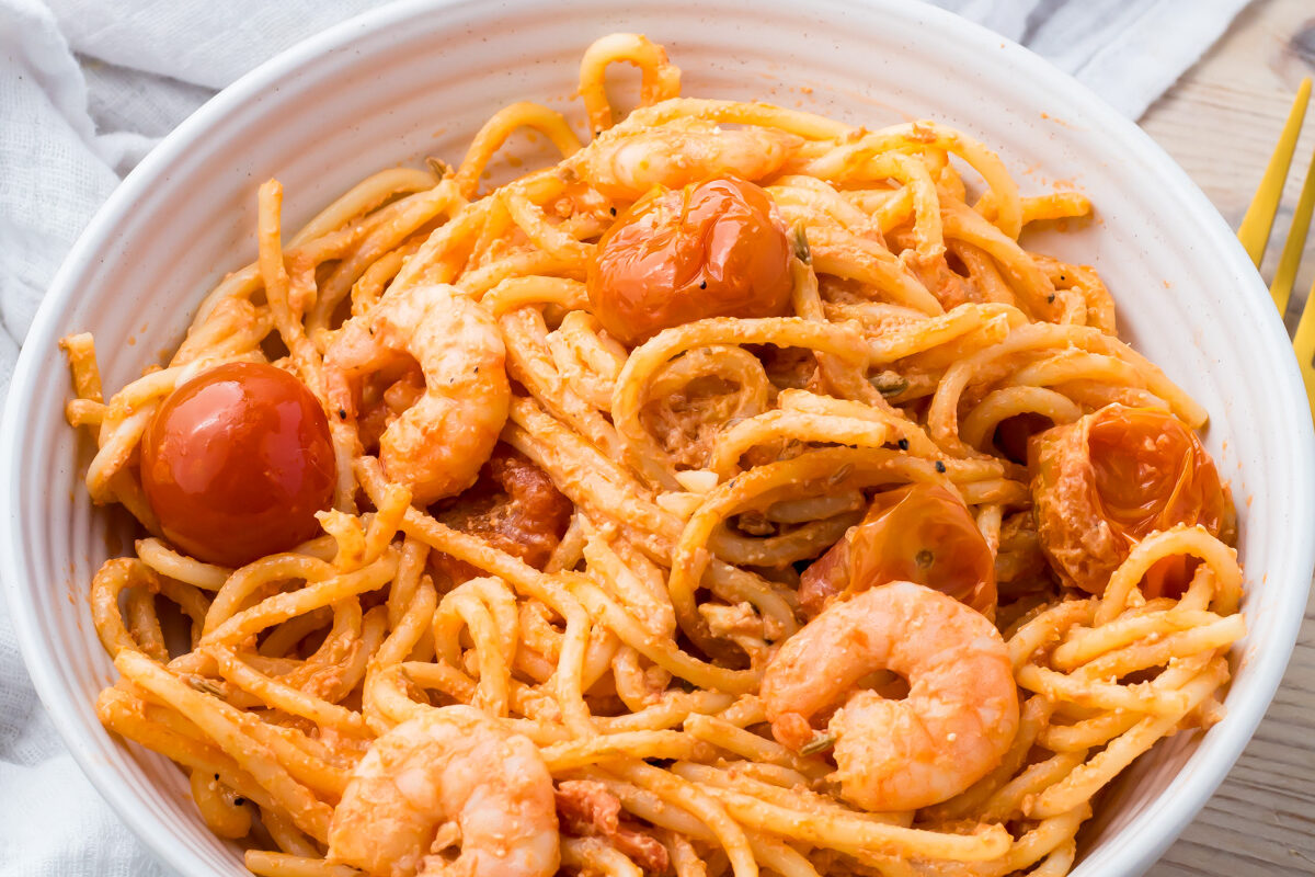 A bowl of shrimp feta pasta with a baking dish of the same pasta in the background.