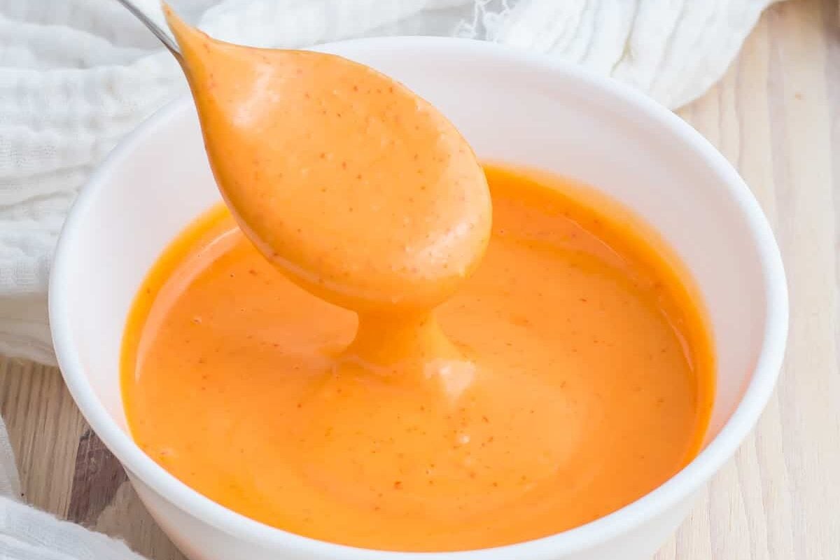 Spoon dripping spicy mayo into a white bowl.