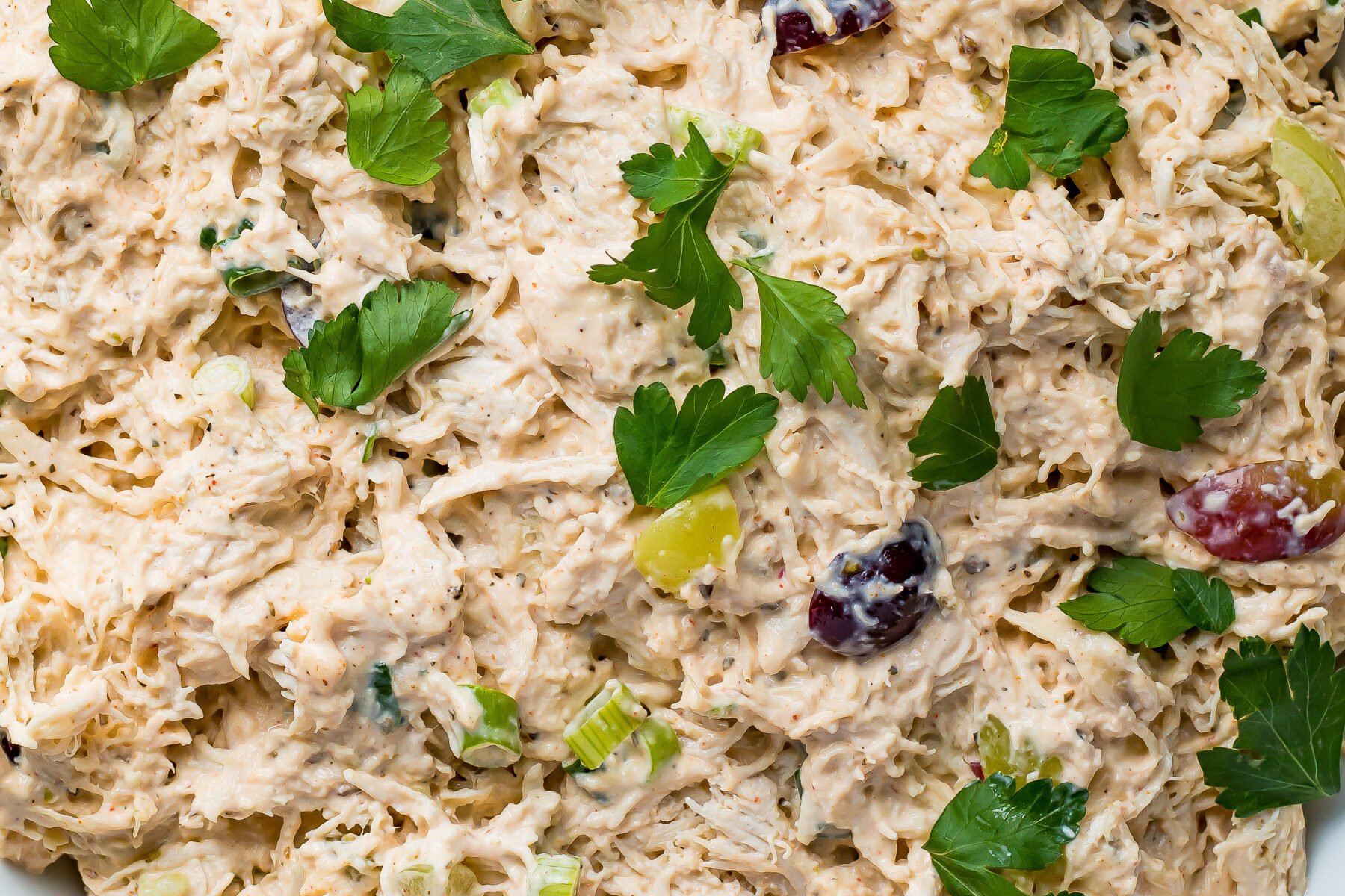 A bowl of chicken salad with grapes and parsley.