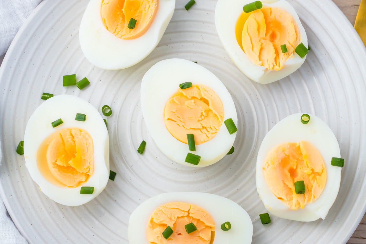 Six halved whole30 hard-boiled eggs arranged on a white plate, garnished with chopped green onions.
