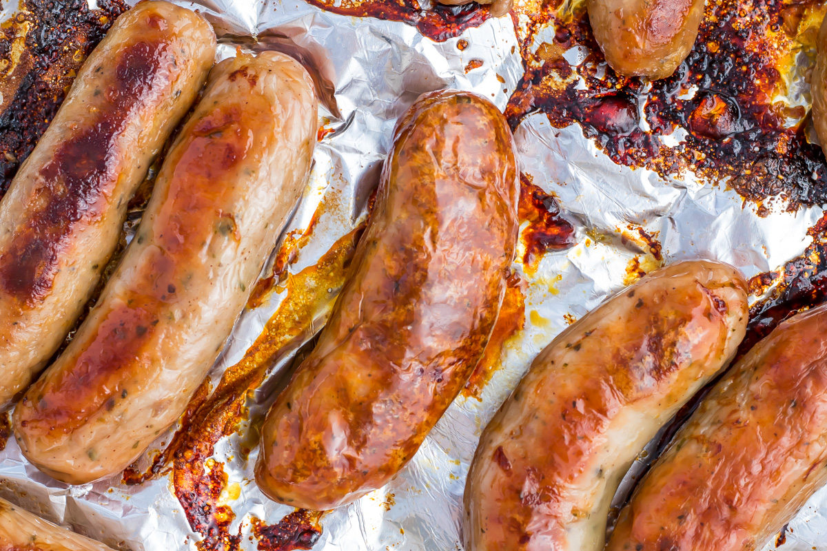 Several cooked sausages on a sheet of crumpled aluminum foil, with browned and caramelized spots visible.