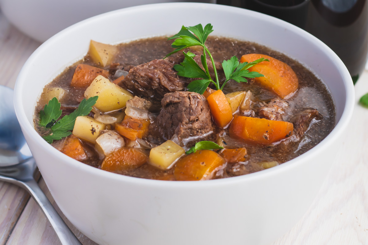 A white bowl filled with beef stew, containing chunks of beef, carrots, potatoes, and garnished with fresh parsley.