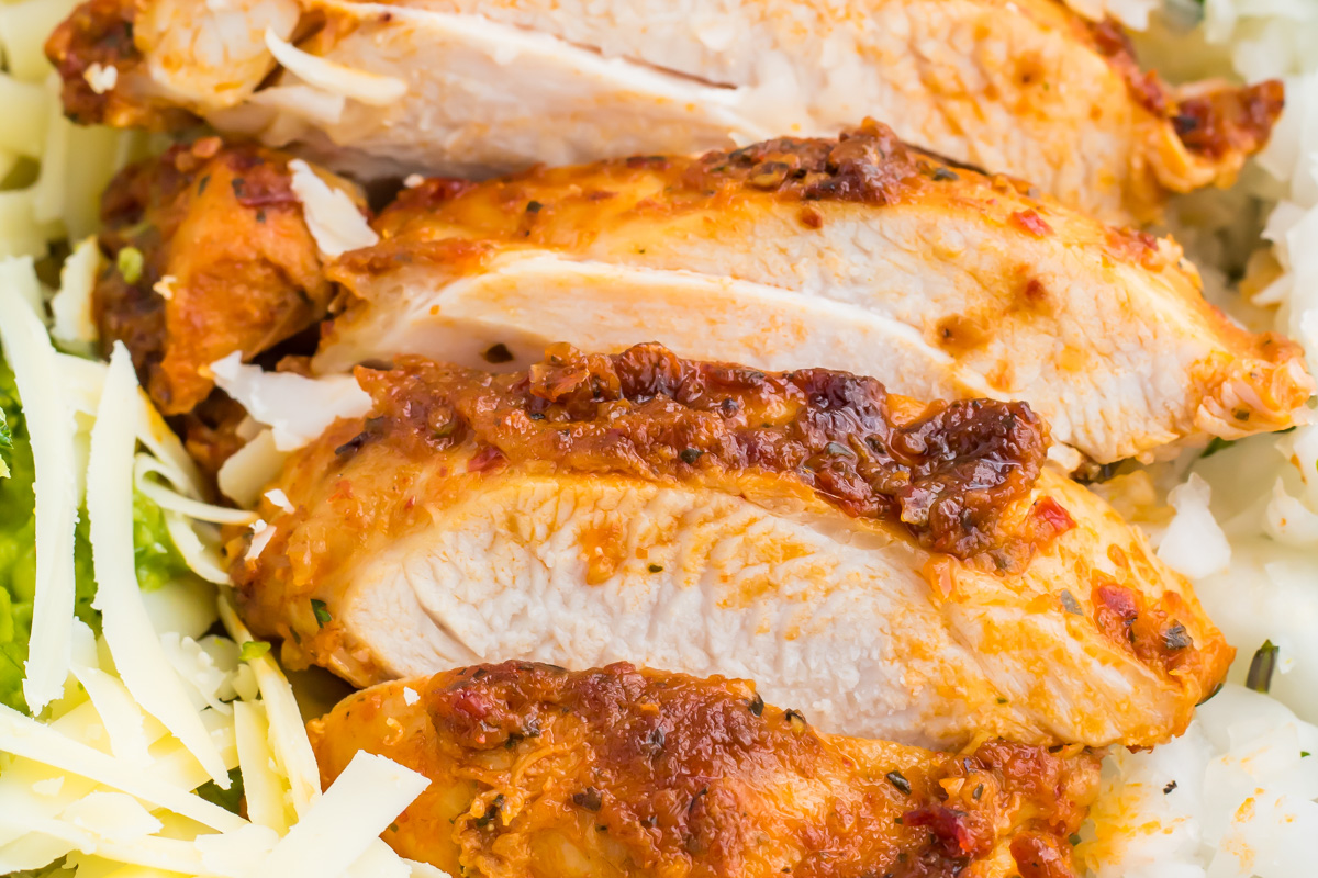 Close-up of sliced, seasoned, cooked chipotle pollo asado with visible spices, served on a bed of shredded cheese and vegetables.