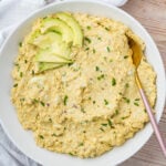 A bowl of creamy cottage cheese avocado egg salad topped with sliced avocado and chopped chives, served with a gold spoon on the side.