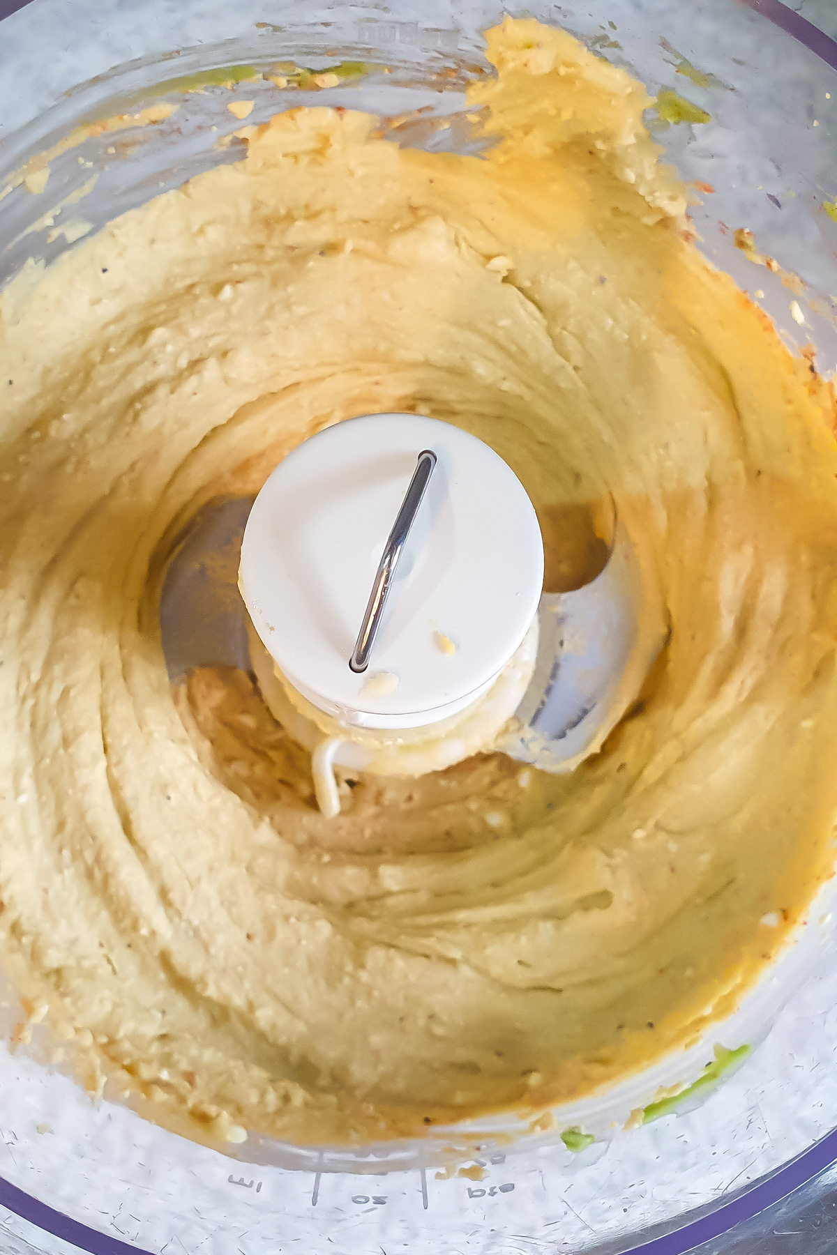 A close-up of a food processor containing a smooth, creamy egg salad mixture, with some remnants clinging to the sides.