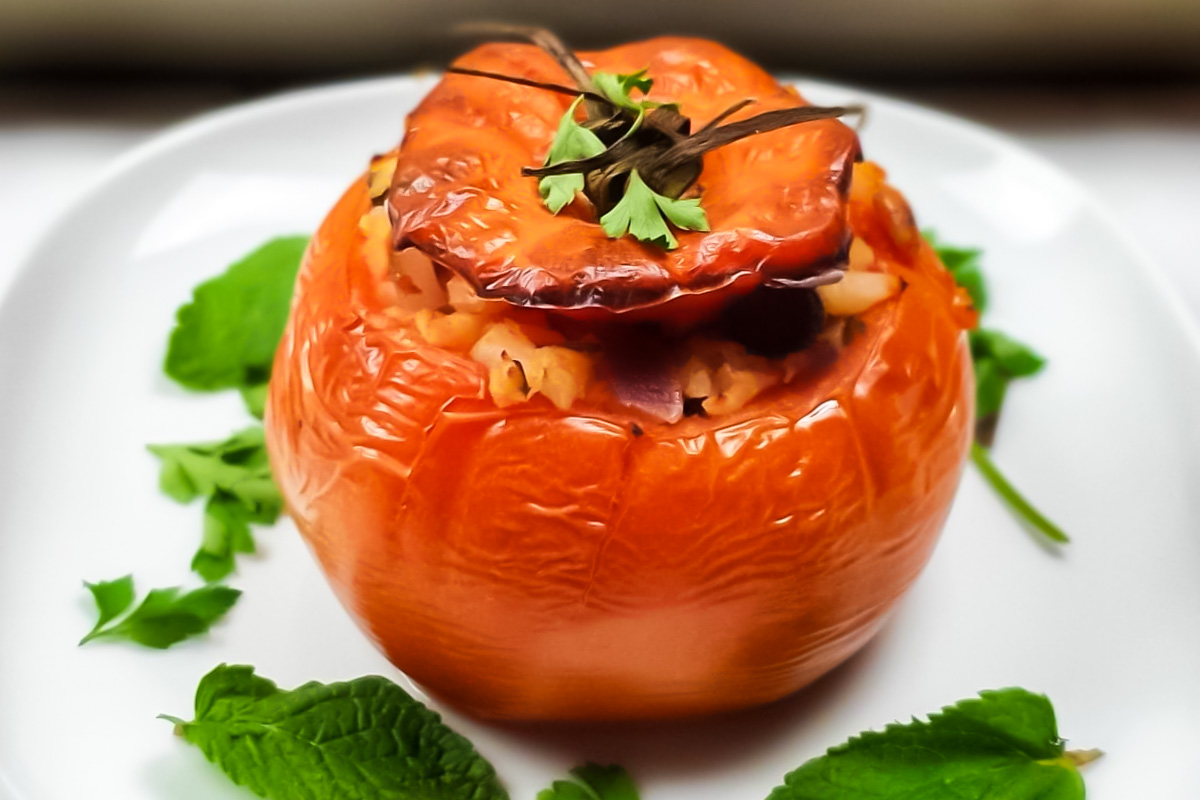 A stuffed tomato filled with cauliflower rice and herbs sits on a white plate, garnished with fresh parsley and mint leaves.
