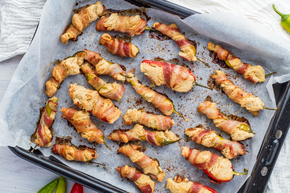 Whole30 bacon-wrapped stuffed jalapeños arranged on a parchment-lined baking tray, freshly baked and lightly browned.