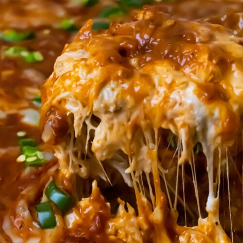 Close-up of a cheesy, saucy casserole with shredded cheese melting and green onions sprinkled on top.
