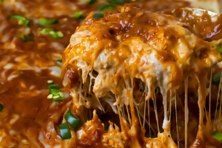 Close-up of a cheesy, saucy casserole with shredded cheese melting and green onions sprinkled on top.
