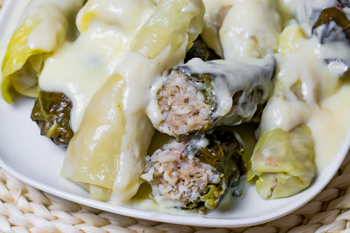 A plate of stuffed cabbage rolls filled with rice and meat, topped with a creamy white sauce, is shown in close-up on a white dish&mdash;perfect for those see.