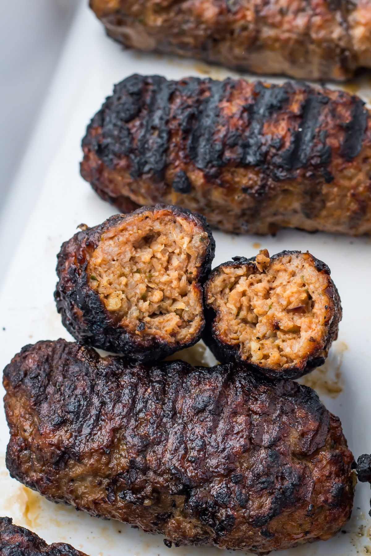 Grilled lamb kofta kebab recipe featuring ground meat kebabs with a charred exterior, one kebab cut in half to reveal the seasoned, cooked interior, all arranged on a white surface.
