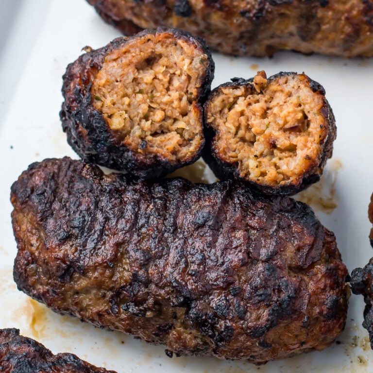 Lamb kofta kebabs, one cut in half to reveal the browned, cooked interior, displayed on a white surface.