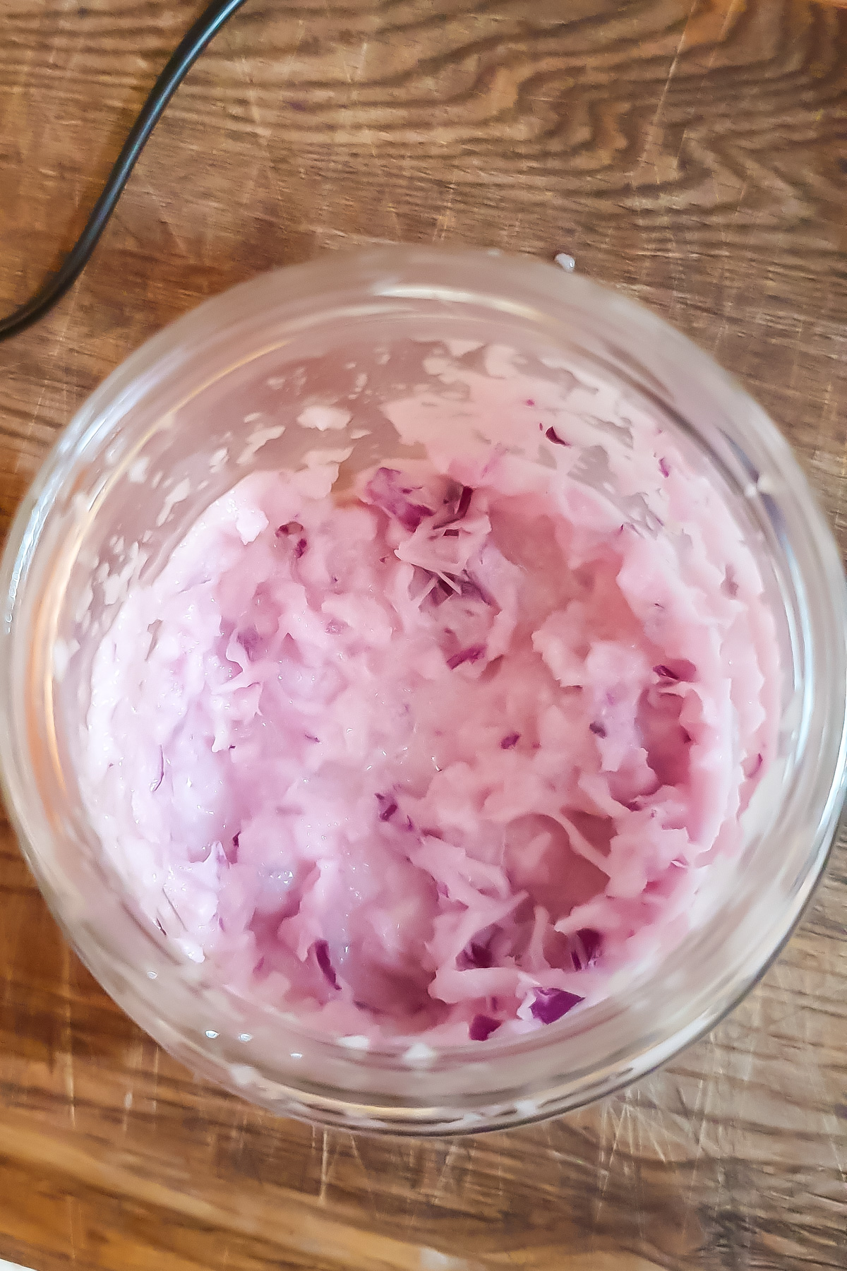 A glass jar containing a mixture of shredded red onion and oil, placed on a wooden surface.