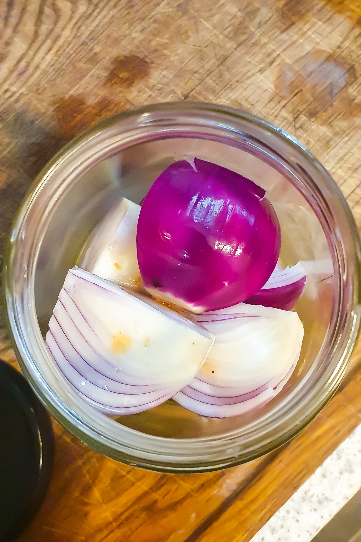 A glass jar containing several wedges of raw red onion, placed on a wooden cutting board.