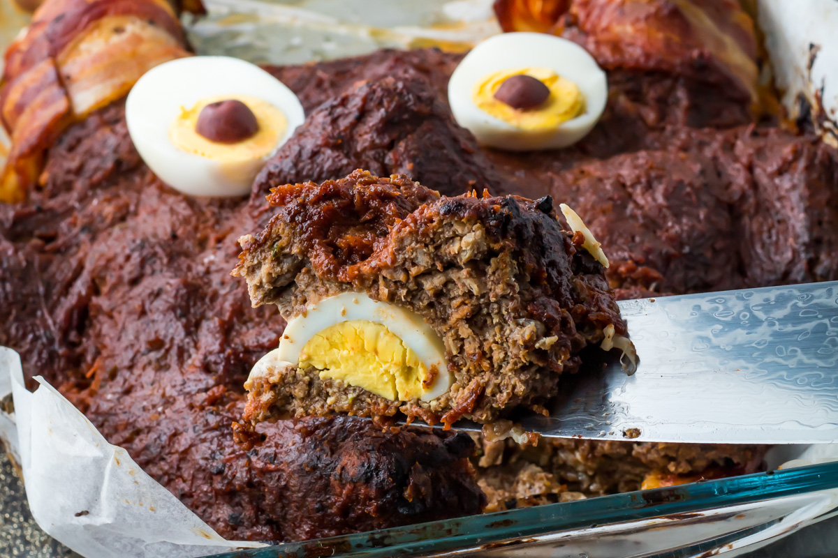 A close-up of a meatloaf shaped like a bear face, with hard-boiled eggs for eyes and a slice revealing an egg inside.