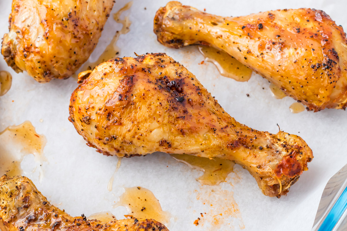 Baked chicken drumsticks with browned, seasoned skin on parchment paper, with visible juices and herbs.