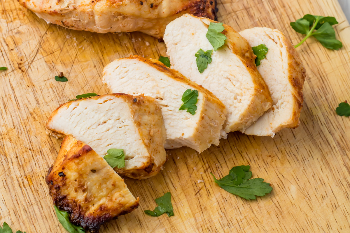 Sliced air fryer whole30 chicken breast on a wooden cutting board, garnished with fresh parsley leaves.