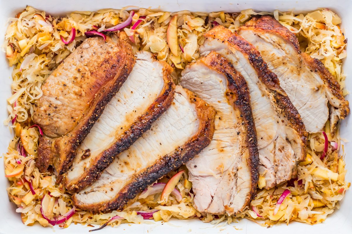 Sliced whole30 air fryer pork with a browned crust placed on a bed of sauerkraut and thinly sliced red onions in a white dish.