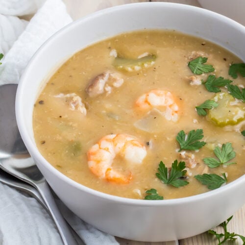 A bowl of whole30 gumbo soup garnished with parsley, featuring a spoon and napkin beside it.