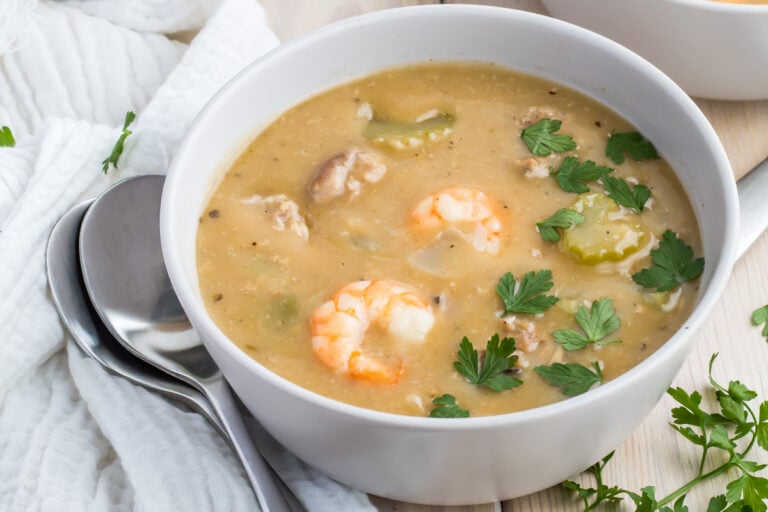 A bowl of whole30 gumbo soup garnished with parsley, featuring a spoon and napkin beside it.