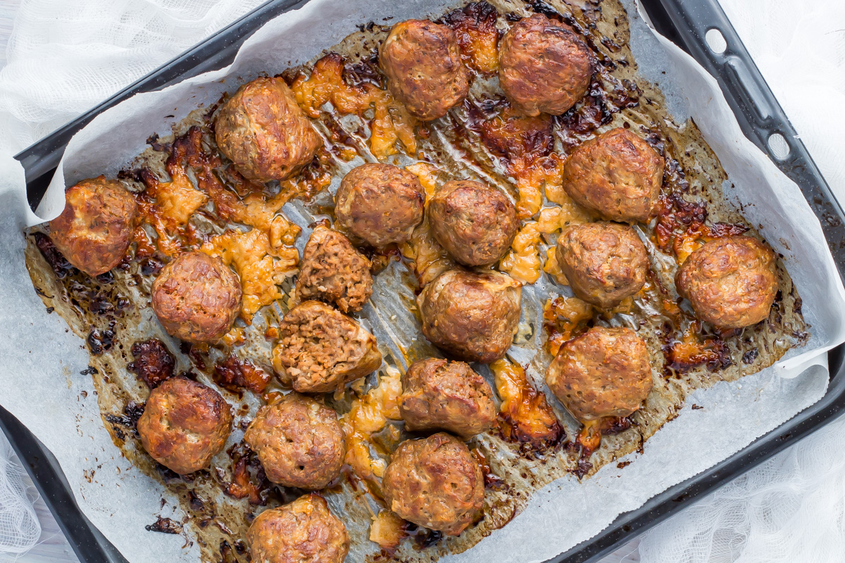 A baking tray lined with parchment paper holds several baked whole30 meatballs, with some browned and crispy spots visible.