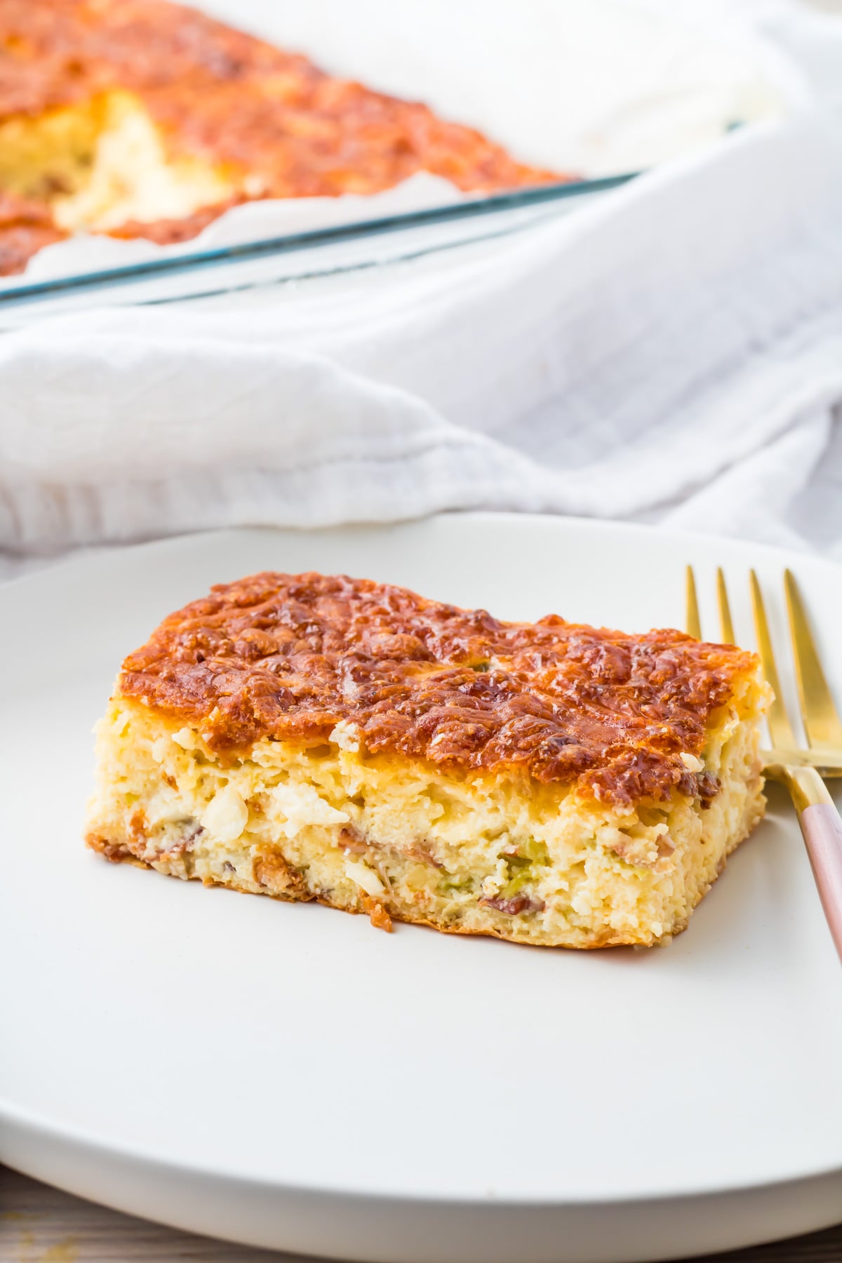 A square slice of cottage cheese egg bake with a golden-brown top is served on a white plate with a fork.