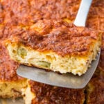 A close-up of a spatula lifting a slice of cottage cheese egg bake with a golden, crispy top and visible pieces of green vegetable inside.