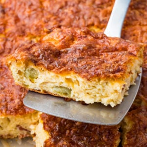 A close-up of a spatula lifting a slice of cottage cheese egg bake with a golden, crispy top and visible pieces of green vegetable inside.