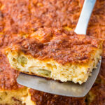 A metal spatula lifts a piece of cottage cheese egg bake with a golden, cheesy crust and visible green pepper pieces.
