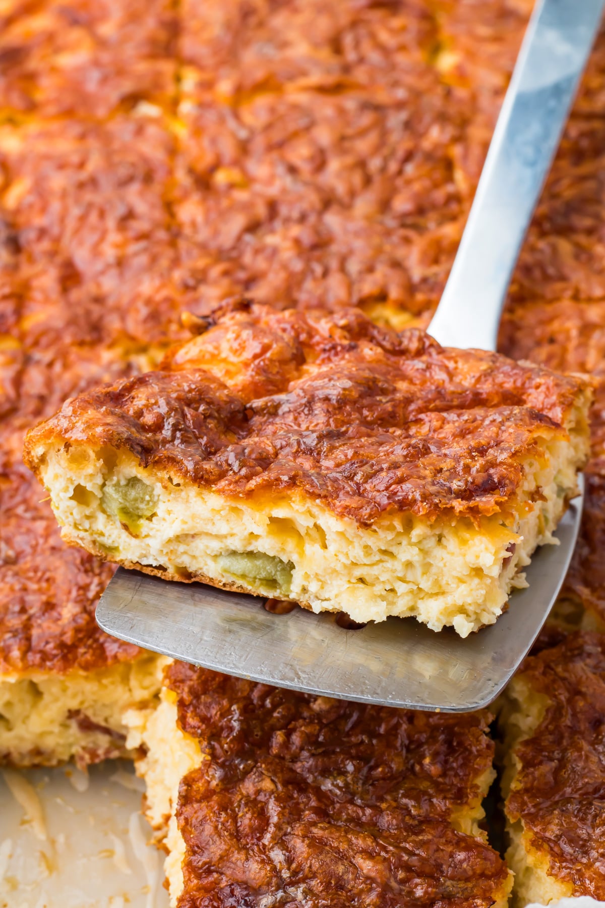A metal spatula lifts a piece of cottage cheese egg bake with a golden, cheesy crust and visible green pepper pieces.