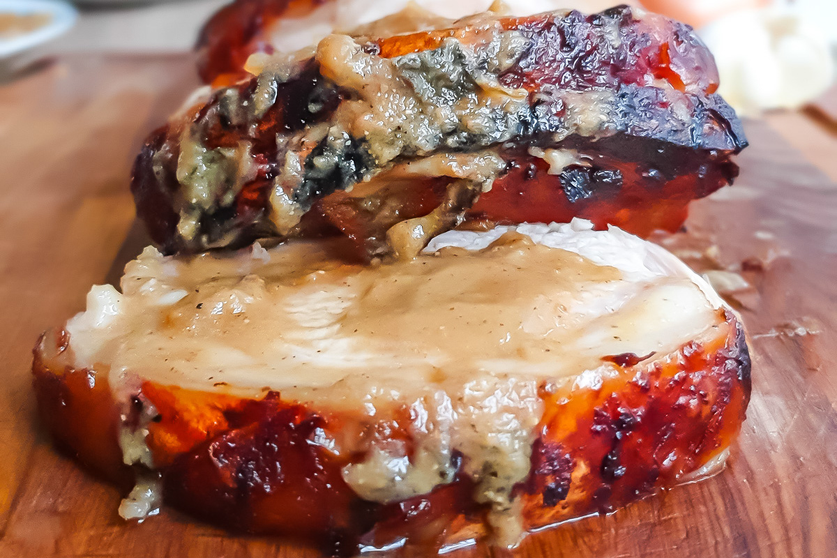 Close-up of thick slices of roasted whole30 pork loin with apple and sage gravy on a wooden cutting board.