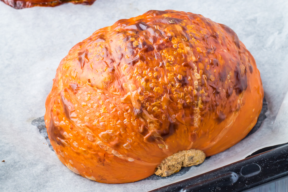 Roasted pumpkin half resting on a parchment-lined baking sheet, with a browned, blistered skin.