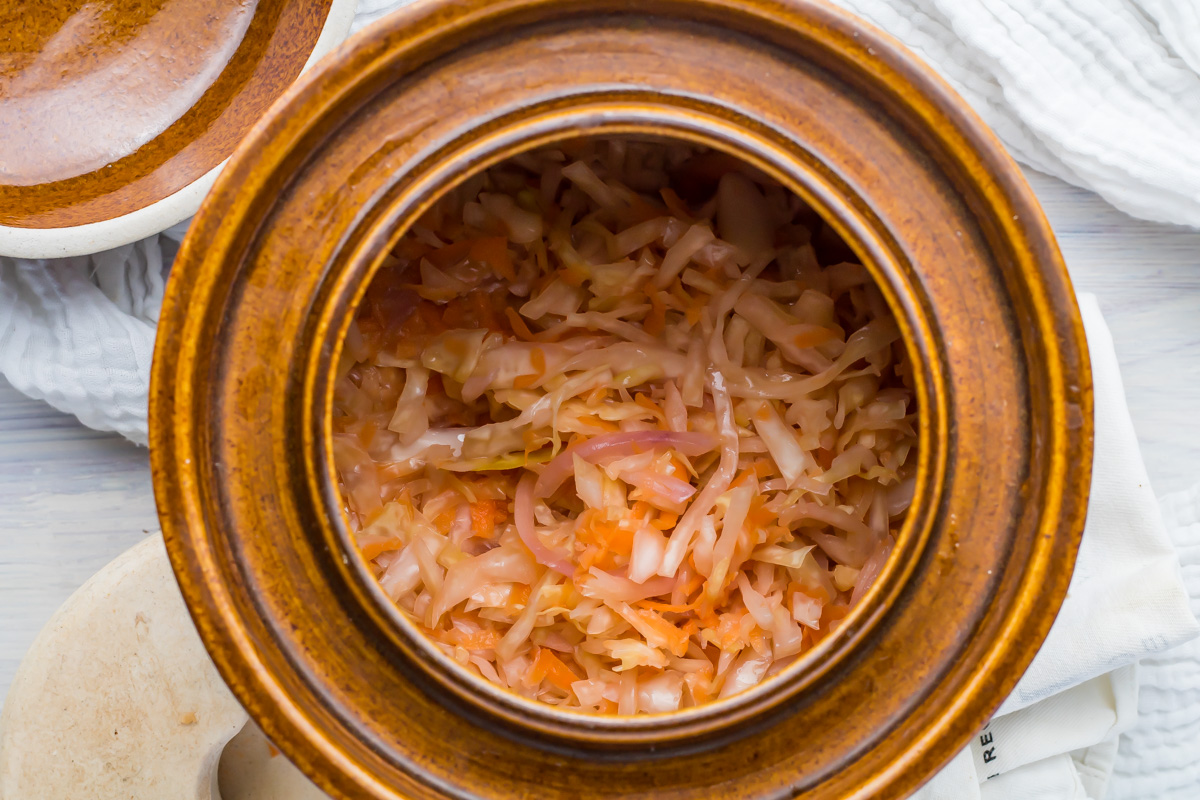 A brown ceramic crock containing shredded fermented sauerkraut.