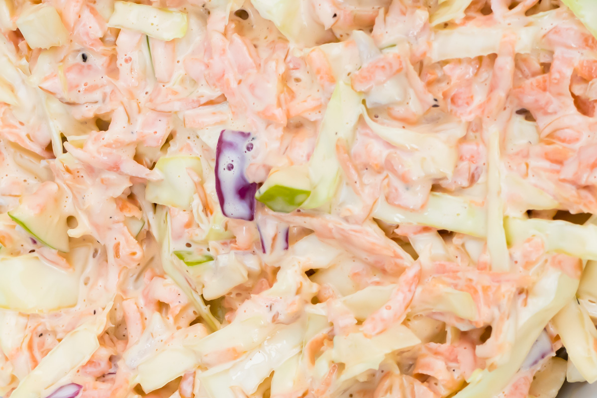 Close-up of creamy whole30 coleslaw with shredded carrots, cabbage, and purple cabbage mixed with dressing.