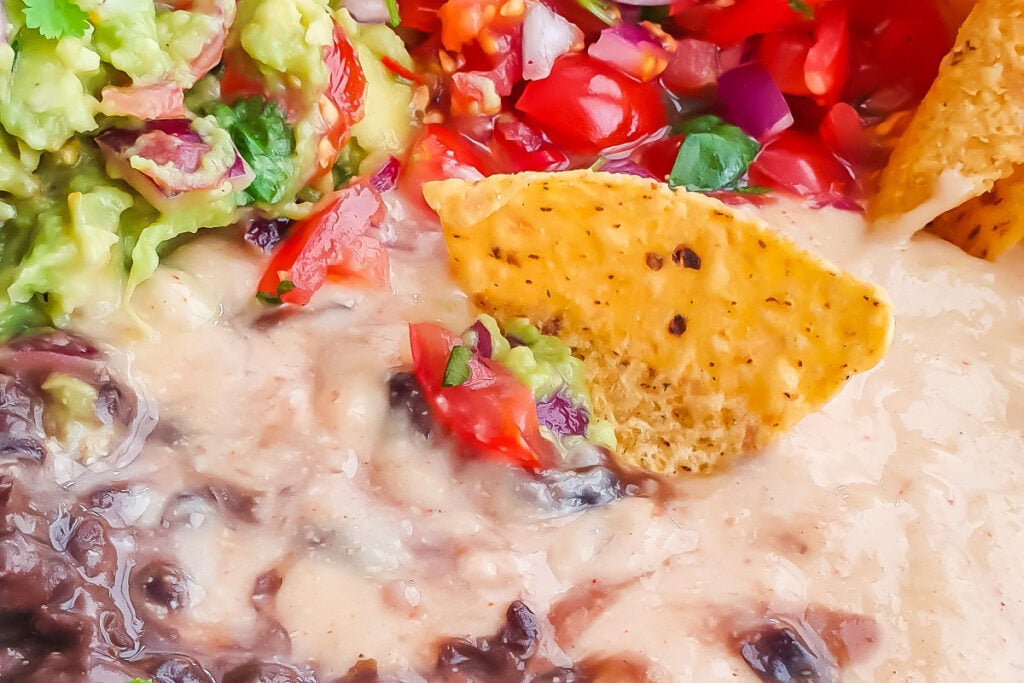 Close-up of nacho chips dipped in whole30 queso, guacamole, black beans, and fresh tomato salsa.
