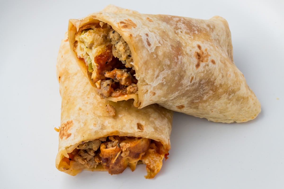 Two breakfast burritos with visible fillings of eggs, sausage, and vegetables on a plain white background.