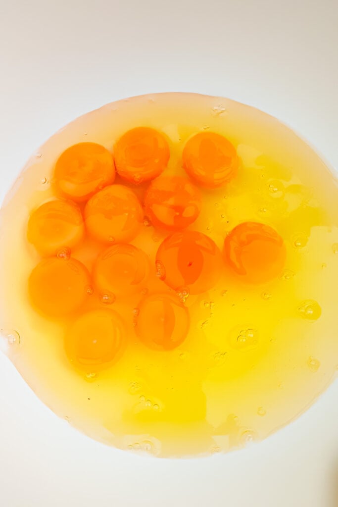 A close-up of several raw egg yolks and egg whites in a clear bowl on a white background, ready to be used for a Cottage Cheese Egg Bake.