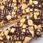 Slab of frozen cottage cheese bark topped with chopped peanuts and drizzled with dark chocolate, cut into squares on parchment paper.