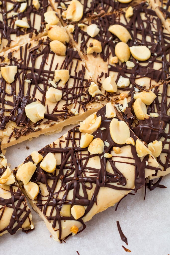 Slab of frozen cottage cheese bark topped with chopped peanuts and drizzled with dark chocolate, cut into squares on parchment paper.