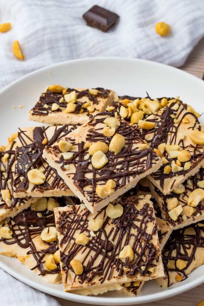 A plate of frozen cottage cheese bark topped with drizzled chocolate and chopped peanuts, arranged on a white plate with a white cloth in the background.