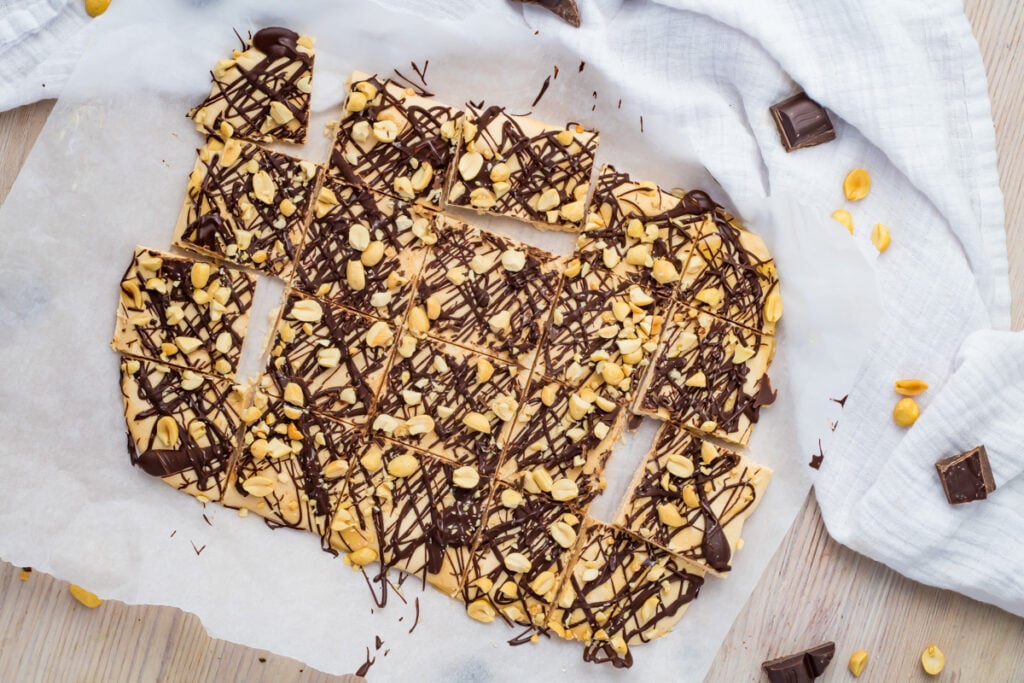 Frozen cottage cheese bark topped with chopped peanuts and drizzled with chocolate, arranged on parchment paper with a few pieces broken off.