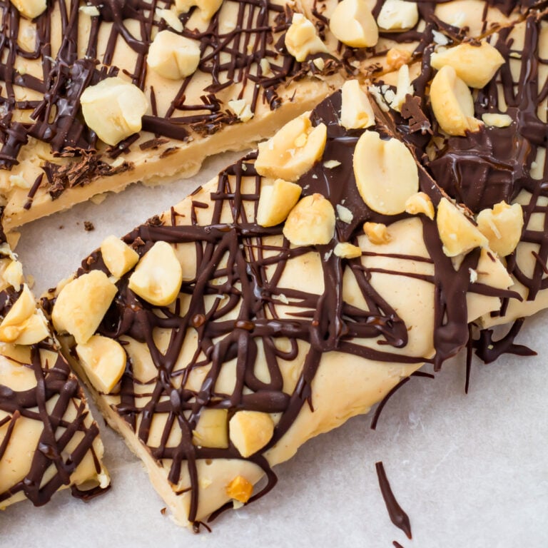 A close-up of frozen cottage cheese bark topped with chopped peanuts and drizzled with dark chocolate on parchment paper.