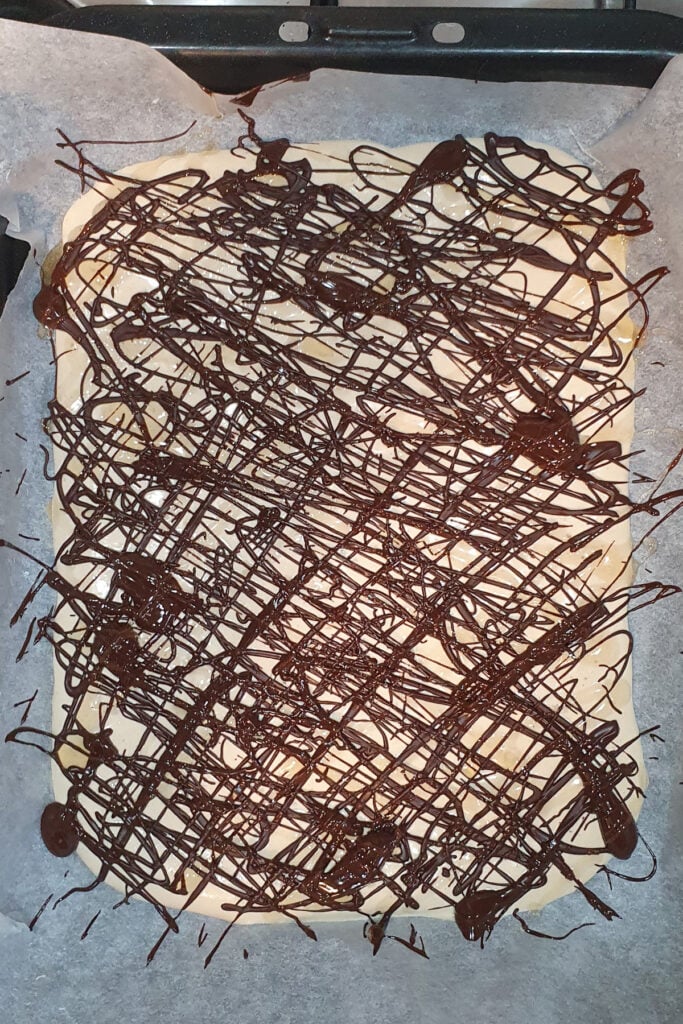 Frozen cottage cheese bark on parchment paper with a random drizzle of melted chocolate on top.
