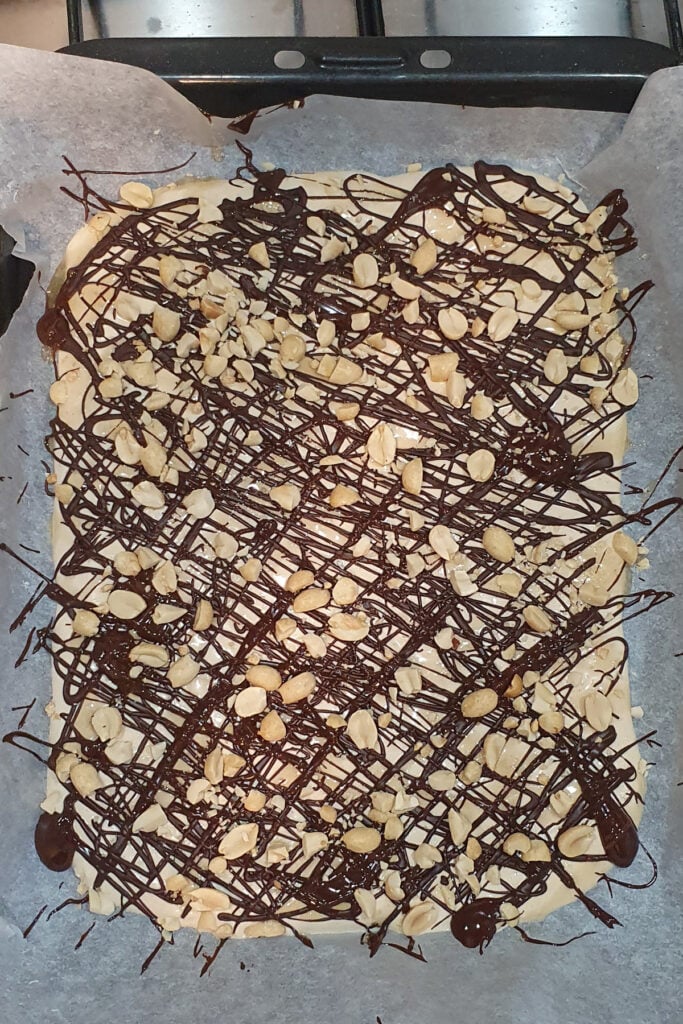 Frozen cottage cheese bark on parchment paper is topped with drizzled chocolate and chopped peanuts.