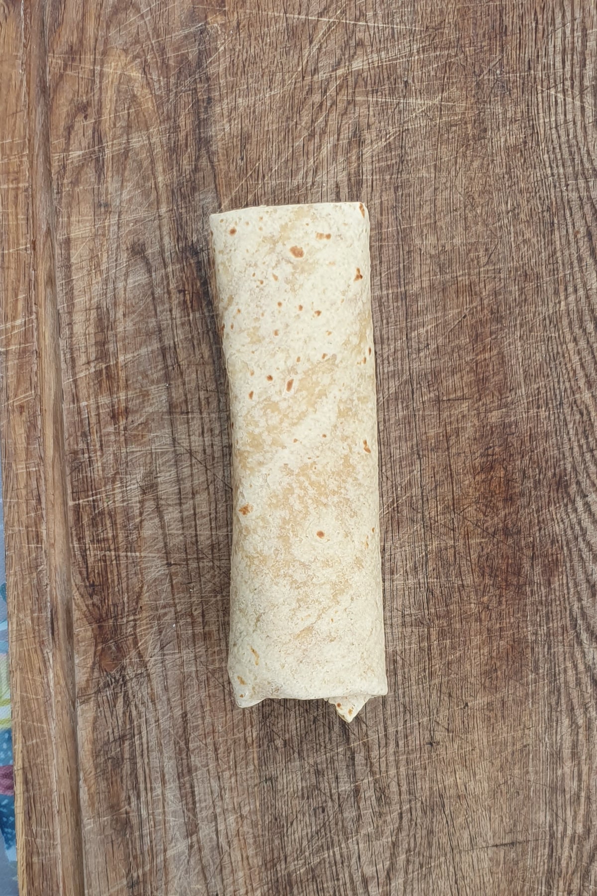 A wrapped burrito placed on a wooden surface.