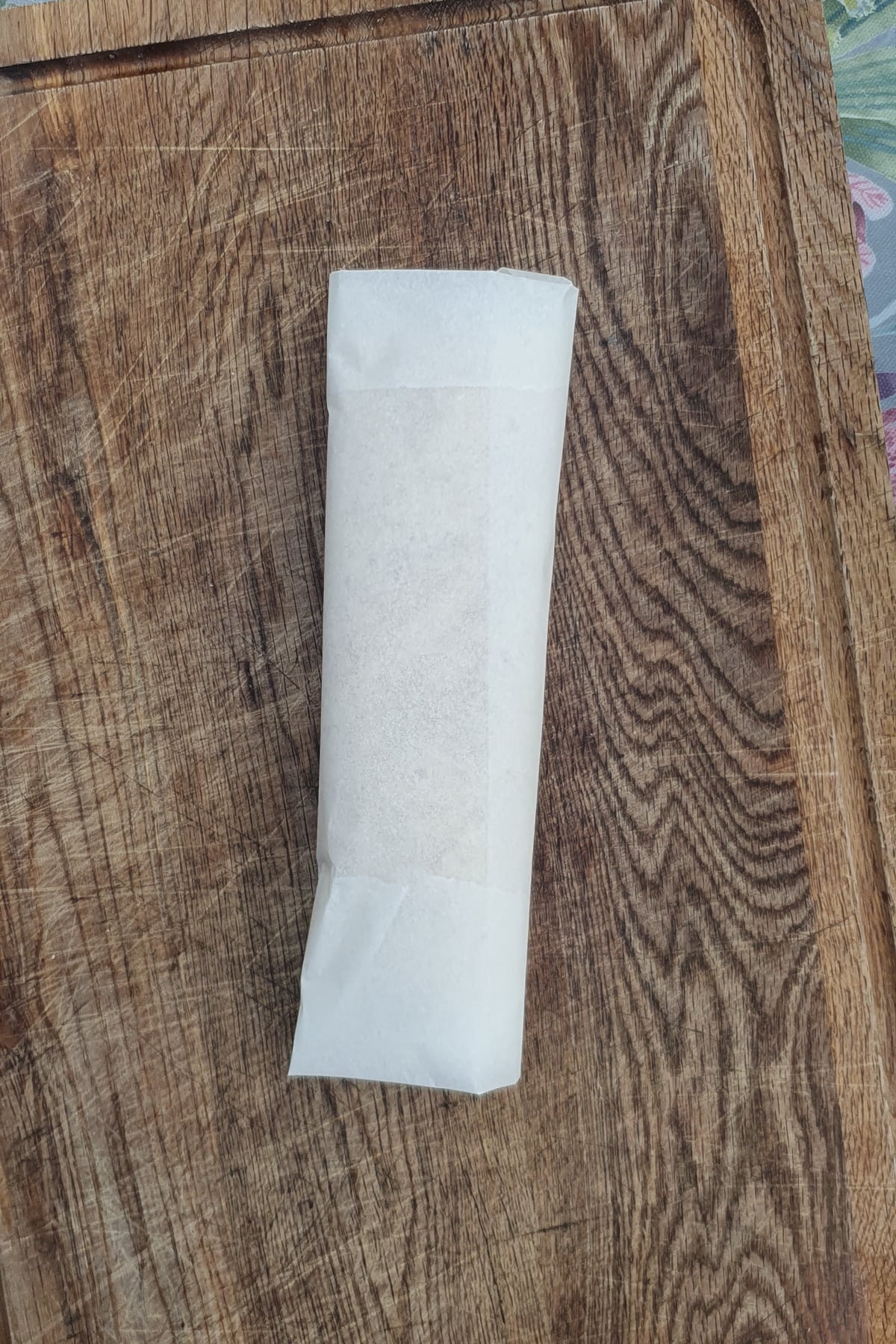A rectangular item wrapped in white paper sits on a wooden cutting board.