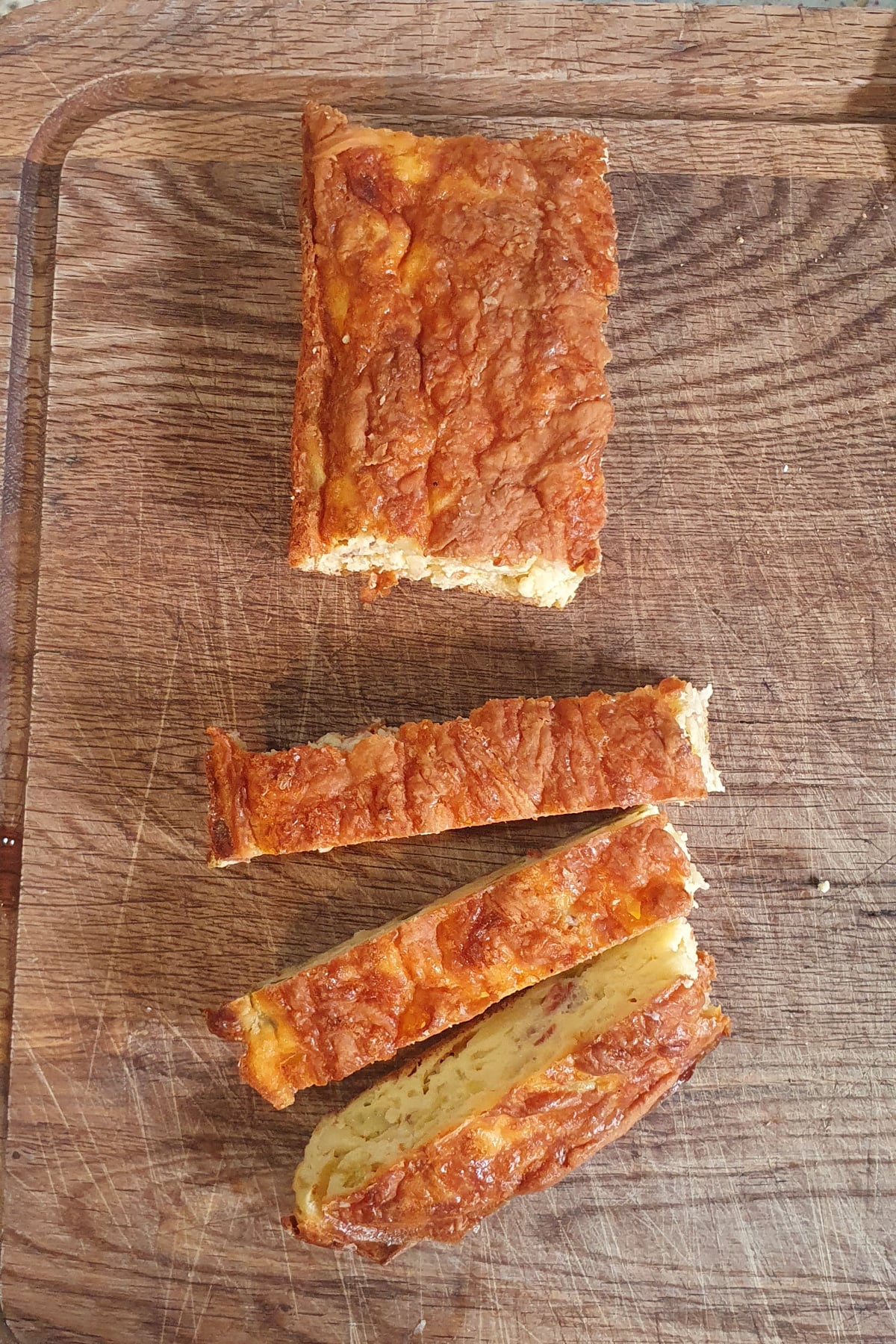 Egg bake with a golden-brown crust is on a wooden cutting board, with two slices cut and laid beside it.