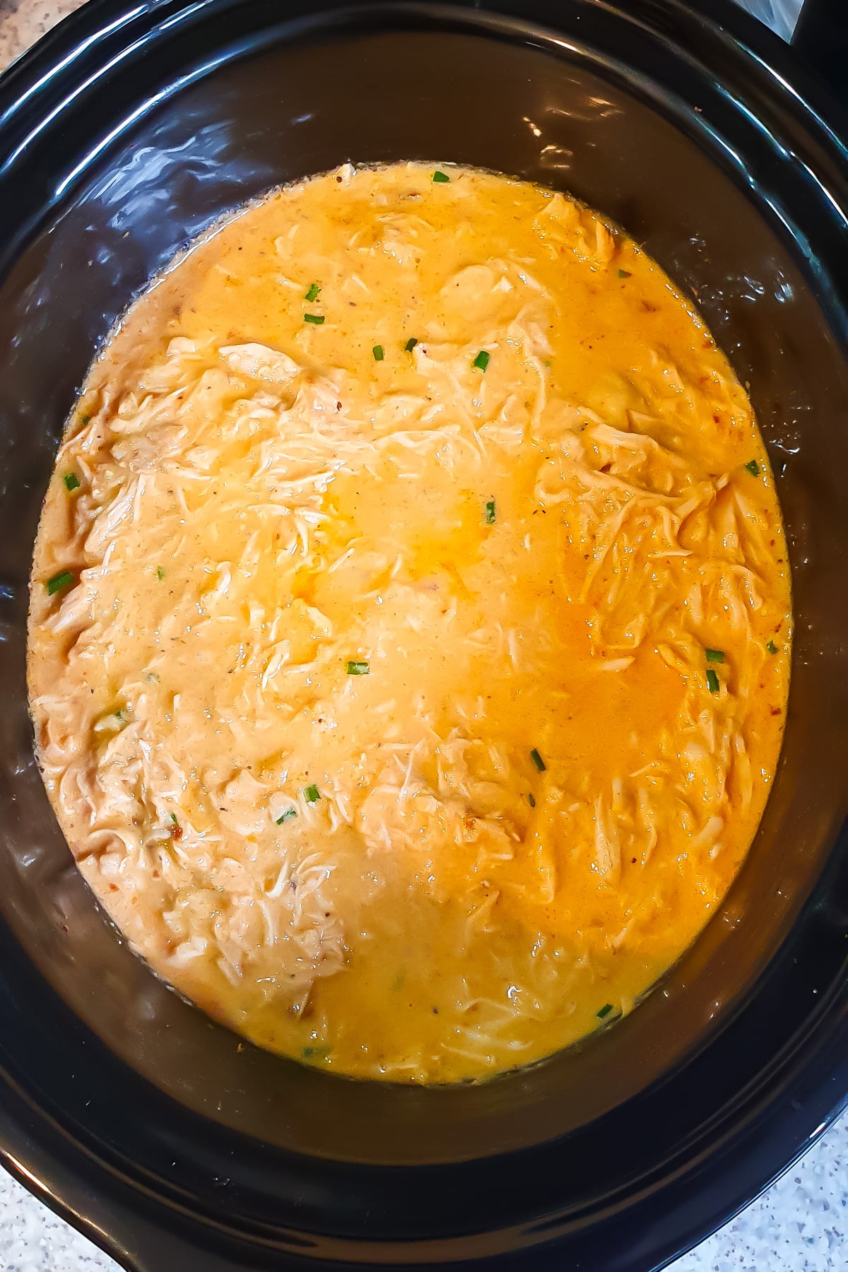 Shredded chicken in a creamy, orange-colored sauce with herbs, cooked in a slow cooker.