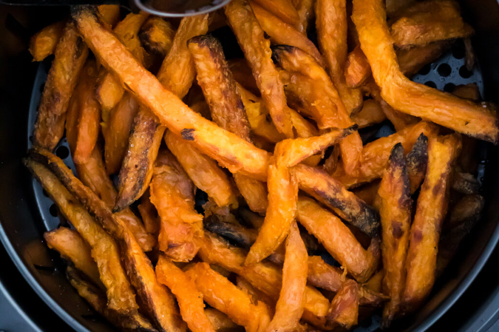 Sweet potato fries in an air fryer basket, cooked to a golden brown with crispy, slightly charred edges.