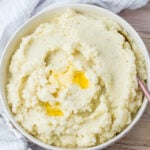 A bowl of cauliflower mash with a pat of melted butter in the center, placed on a light-colored cloth.